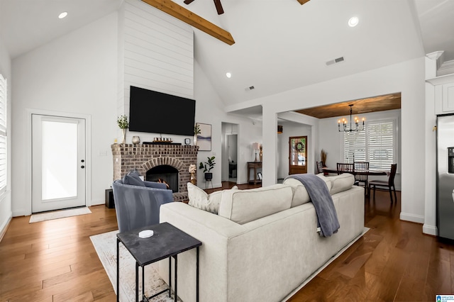 living room featuring high vaulted ceiling, ceiling fan with notable chandelier, a fireplace, beam ceiling, and hardwood / wood-style flooring