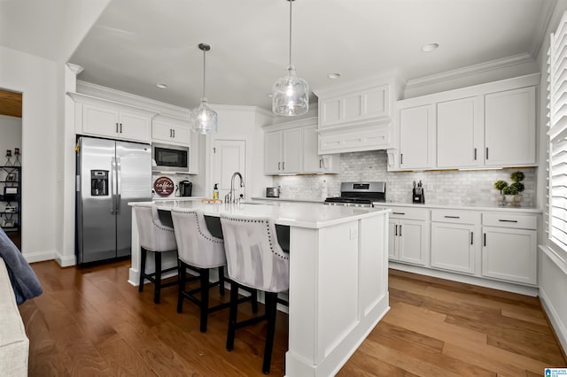 kitchen with appliances with stainless steel finishes, an island with sink, white cabinets, decorative light fixtures, and hardwood / wood-style floors