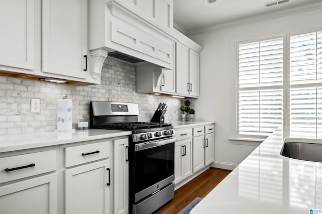 kitchen featuring white cabinetry, backsplash, dark hardwood / wood-style flooring, stainless steel gas stove, and ornamental molding