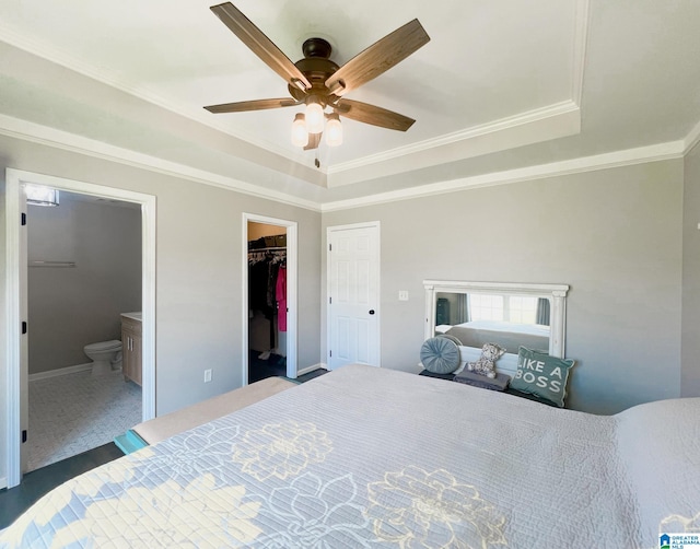 carpeted bedroom featuring a tray ceiling, ornamental molding, connected bathroom, a spacious closet, and ceiling fan