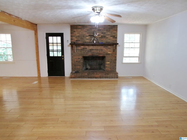 unfurnished living room with light hardwood / wood-style flooring, a brick fireplace, and plenty of natural light