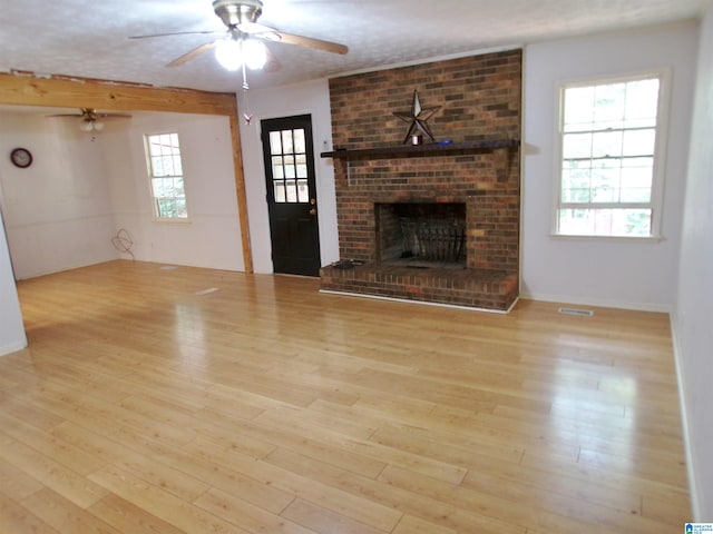 unfurnished living room featuring a wealth of natural light, light hardwood / wood-style floors, a fireplace, and ceiling fan