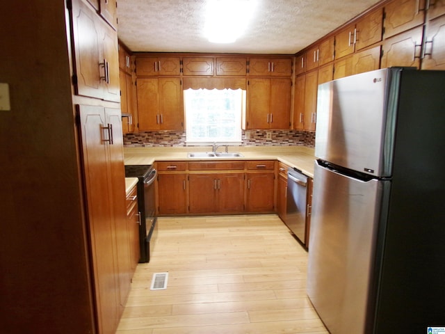 kitchen with a textured ceiling, stainless steel appliances, light wood-type flooring, and sink