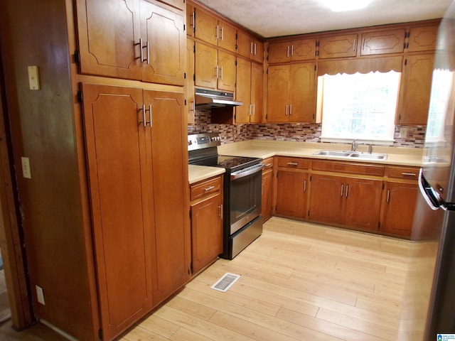 kitchen with sink, a textured ceiling, stainless steel appliances, light hardwood / wood-style floors, and decorative backsplash