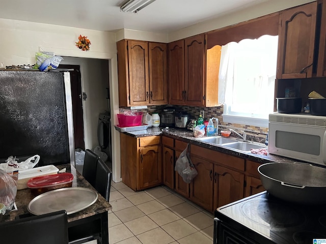 kitchen with black refrigerator, sink, light tile patterned flooring, backsplash, and washer / dryer