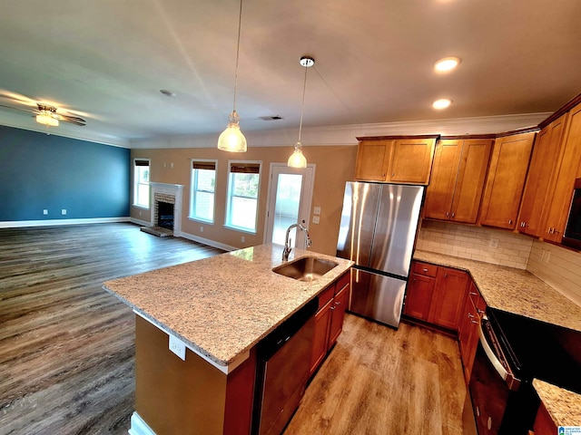 kitchen featuring light hardwood / wood-style flooring, stainless steel appliances, a center island with sink, and light stone countertops