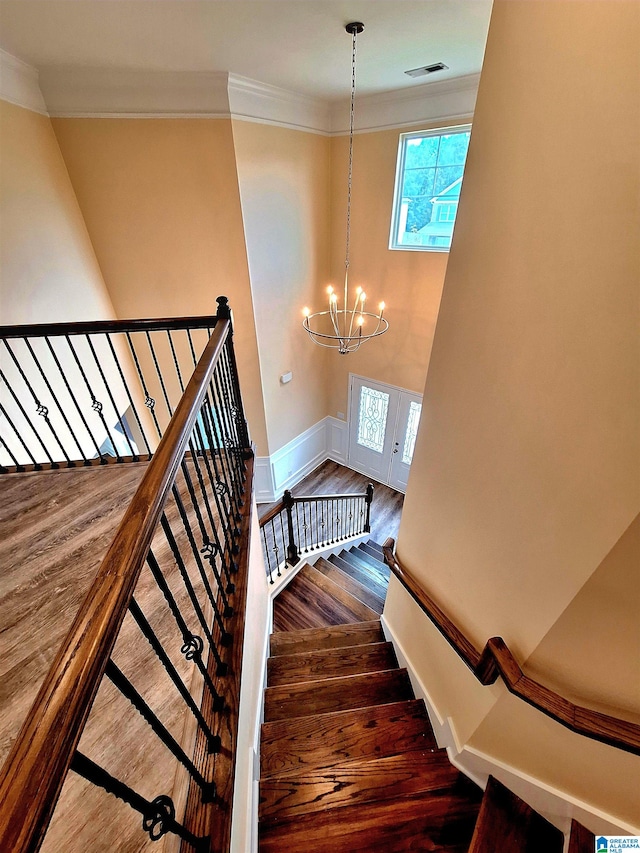 stairs with wood-type flooring, crown molding, and a chandelier