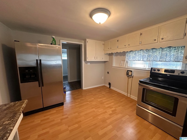 kitchen featuring light wood-type flooring, dark stone counters, white cabinetry, and stainless steel appliances