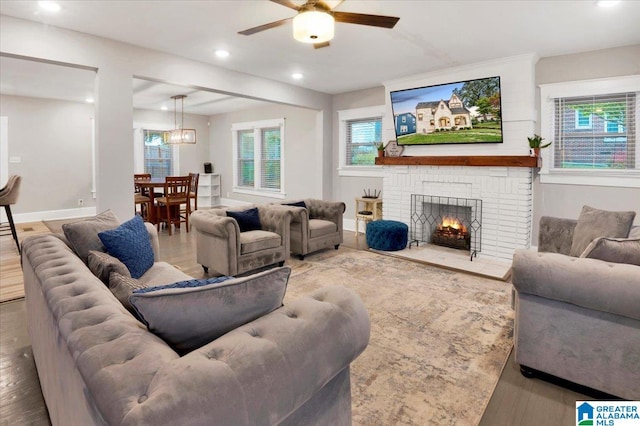 living room featuring wood-type flooring, a brick fireplace, and ceiling fan