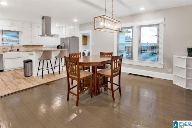 dining space featuring an inviting chandelier, hardwood / wood-style floors, separate washer and dryer, and sink