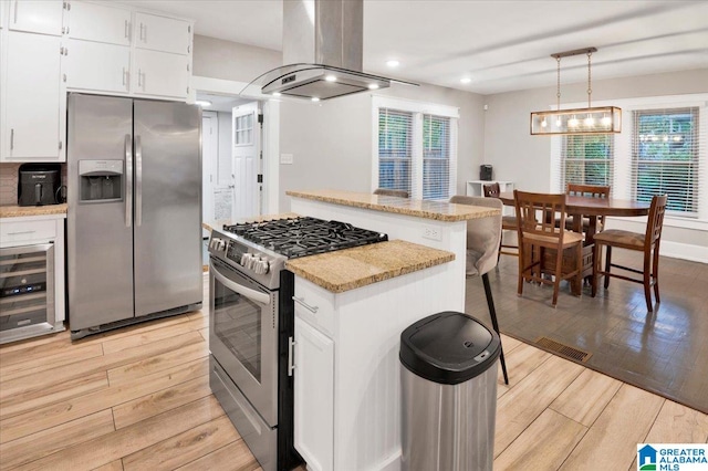 kitchen featuring white cabinets, island exhaust hood, appliances with stainless steel finishes, and hanging light fixtures