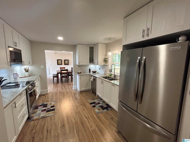 kitchen featuring appliances with stainless steel finishes, light hardwood / wood-style floors, white cabinetry, pendant lighting, and sink