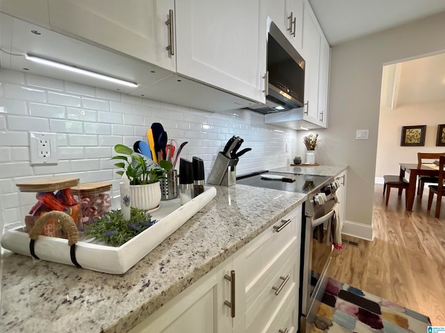 kitchen featuring light stone countertops, backsplash, white cabinetry, appliances with stainless steel finishes, and light wood-type flooring