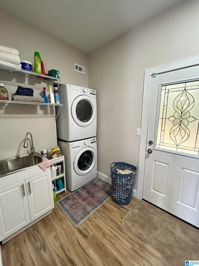 washroom with stacked washer / dryer, wood-type flooring, sink, and cabinets