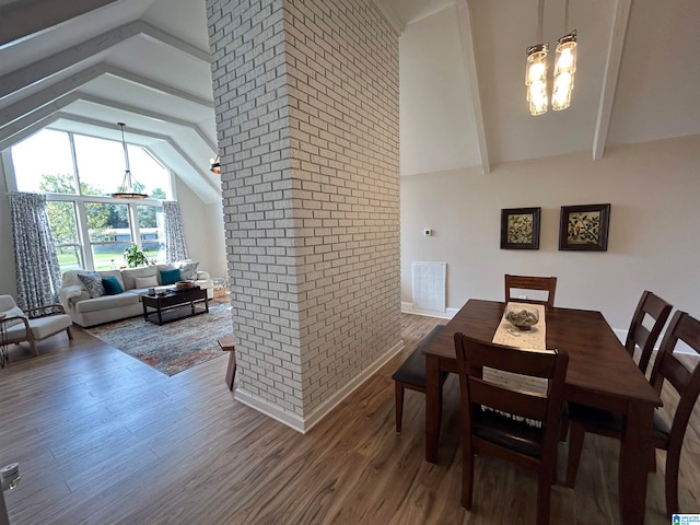 dining room featuring brick wall, vaulted ceiling with beams, a notable chandelier, and hardwood / wood-style floors