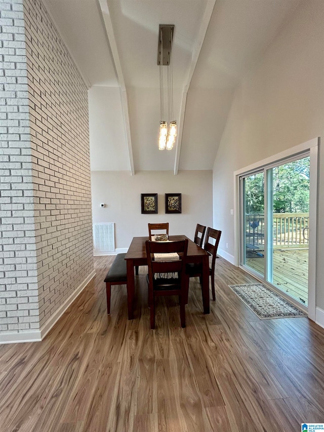 dining room featuring brick wall, hardwood / wood-style flooring, lofted ceiling with beams, and a chandelier