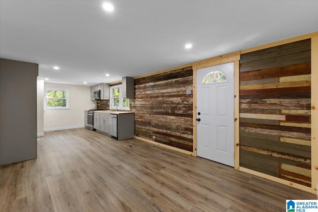 kitchen featuring wood walls, gray cabinets, light hardwood / wood-style flooring, sink, and stainless steel appliances