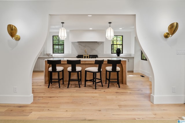 kitchen featuring a kitchen breakfast bar, white cabinets, light wood-type flooring, and decorative light fixtures