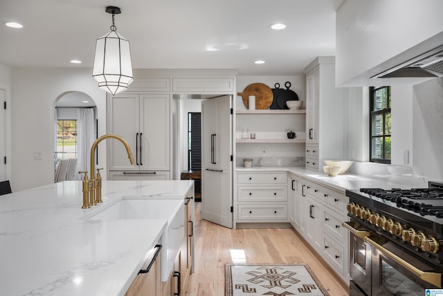 kitchen featuring pendant lighting, light stone counters, light hardwood / wood-style floors, white cabinets, and double oven range