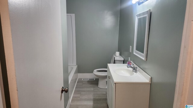 bathroom featuring a tub to relax in, wood-type flooring, vanity, and toilet