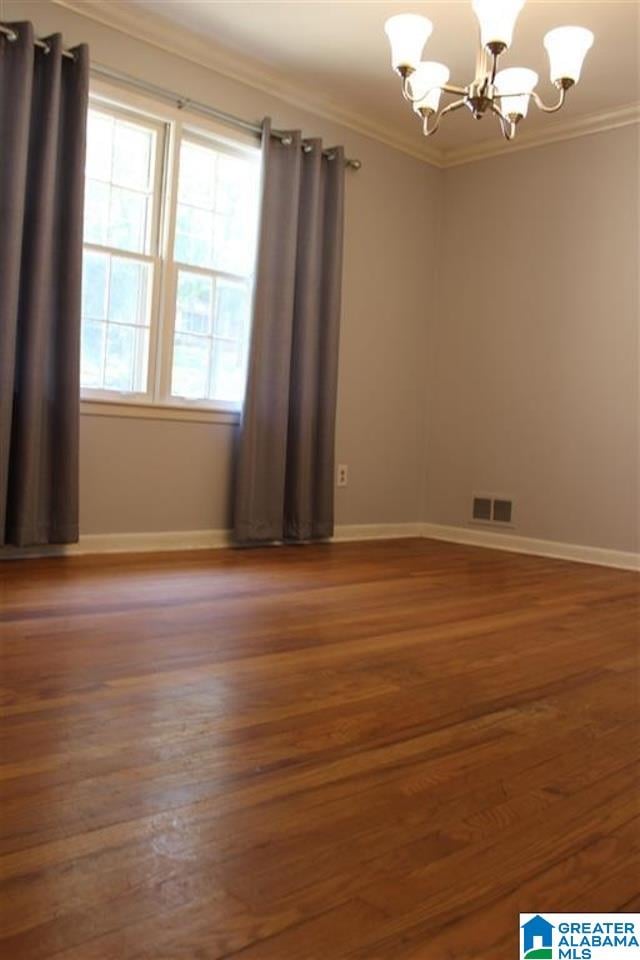 spare room featuring a notable chandelier, crown molding, and dark wood-type flooring