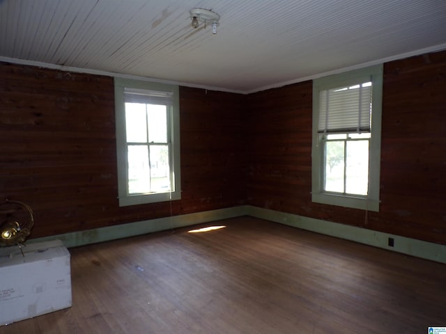 empty room with wooden walls, wood finished floors, and ornamental molding