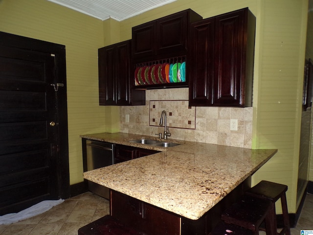 kitchen featuring a peninsula, a sink, a kitchen bar, light stone counters, and dishwasher
