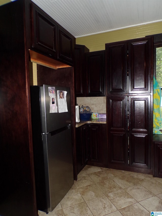 kitchen with light stone countertops, freestanding refrigerator, dark brown cabinetry, and backsplash