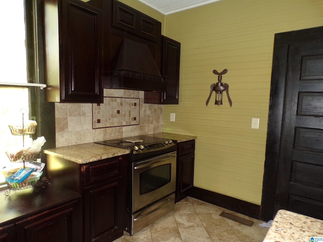 kitchen with premium range hood, backsplash, dark brown cabinetry, and electric stove