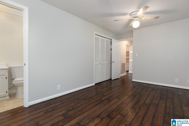 unfurnished bedroom with ceiling fan, a textured ceiling, dark wood-type flooring, a closet, and ensuite bathroom