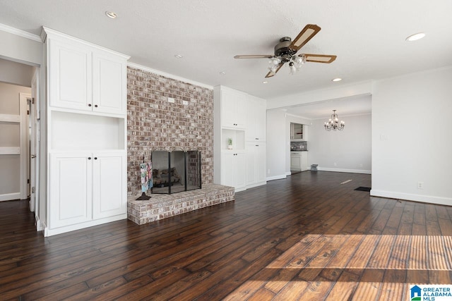 unfurnished living room with ceiling fan with notable chandelier, a brick fireplace, crown molding, and dark hardwood / wood-style flooring