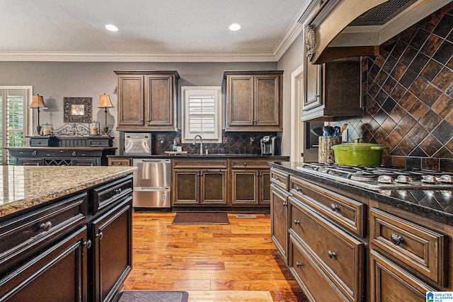 kitchen with dark stone counters, light hardwood / wood-style floors, range hood, decorative backsplash, and ornamental molding