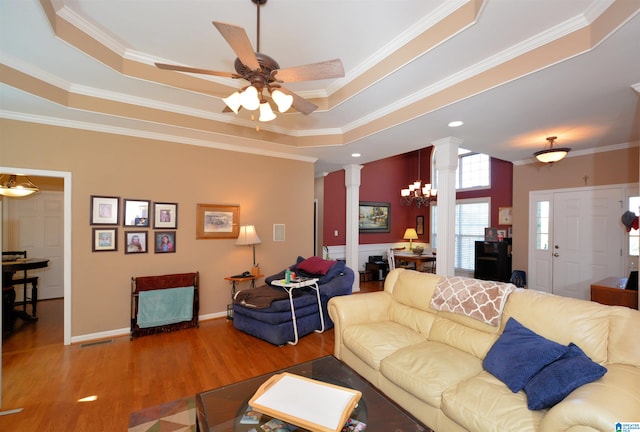 living room with ceiling fan with notable chandelier, a raised ceiling, hardwood / wood-style floors, ornate columns, and crown molding