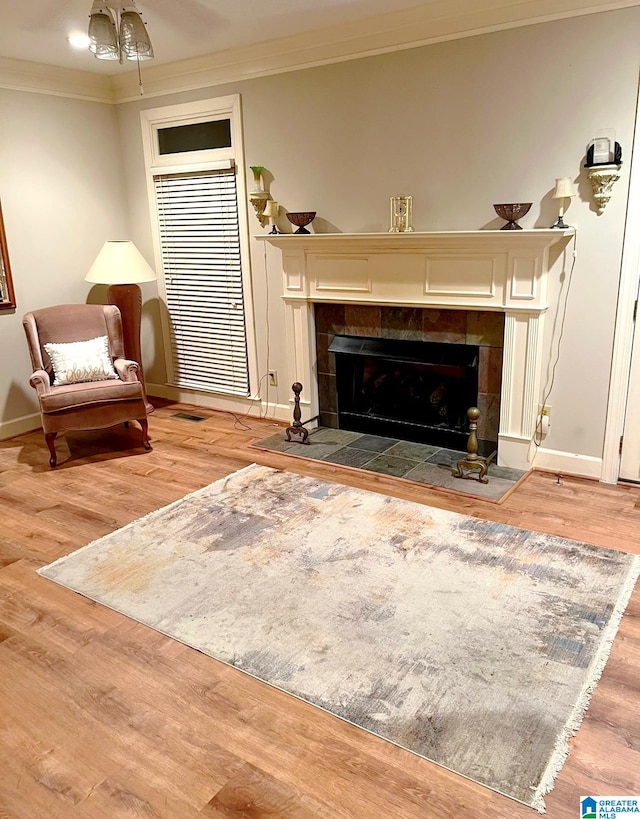 living area with crown molding, wood-type flooring, and a tile fireplace