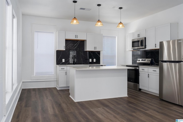 kitchen featuring hanging light fixtures, appliances with stainless steel finishes, a kitchen island, and white cabinetry