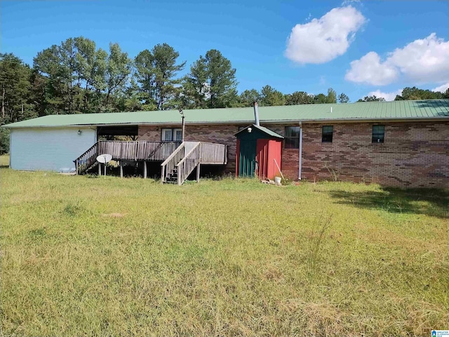 rear view of property with a wooden deck, a lawn, brick siding, and a storage shed