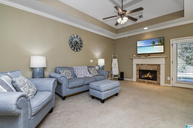 living room featuring a tile fireplace, light carpet, a raised ceiling, crown molding, and ceiling fan