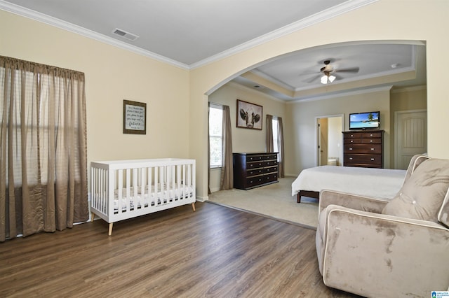 bedroom with ceiling fan, a tray ceiling, crown molding, and hardwood / wood-style floors