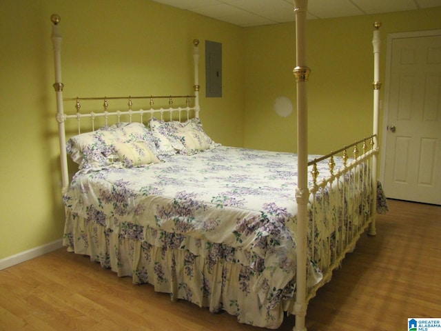 bedroom with a drop ceiling, electric panel, and hardwood / wood-style flooring