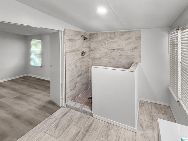 bathroom featuring a textured ceiling, a tile shower, vaulted ceiling, and hardwood / wood-style floors