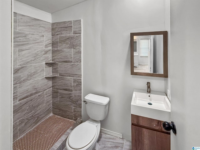 bathroom featuring a tile shower, vanity, and toilet