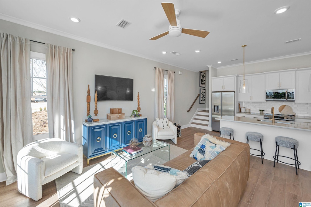 living room featuring ornamental molding, light wood-type flooring, ceiling fan, and sink