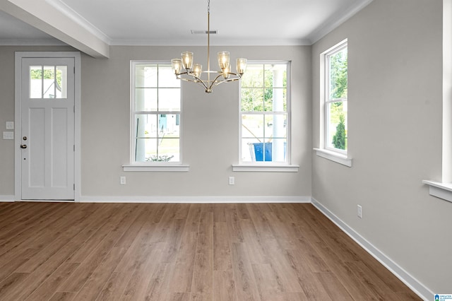 unfurnished dining area with a wealth of natural light, ornamental molding, wood-type flooring, and an inviting chandelier