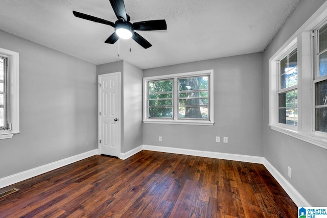 unfurnished bedroom with dark wood-type flooring, a textured ceiling, multiple windows, and ceiling fan