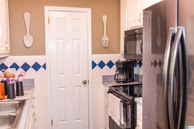 kitchen featuring tile walls, white cabinets, black appliances, decorative light fixtures, and sink