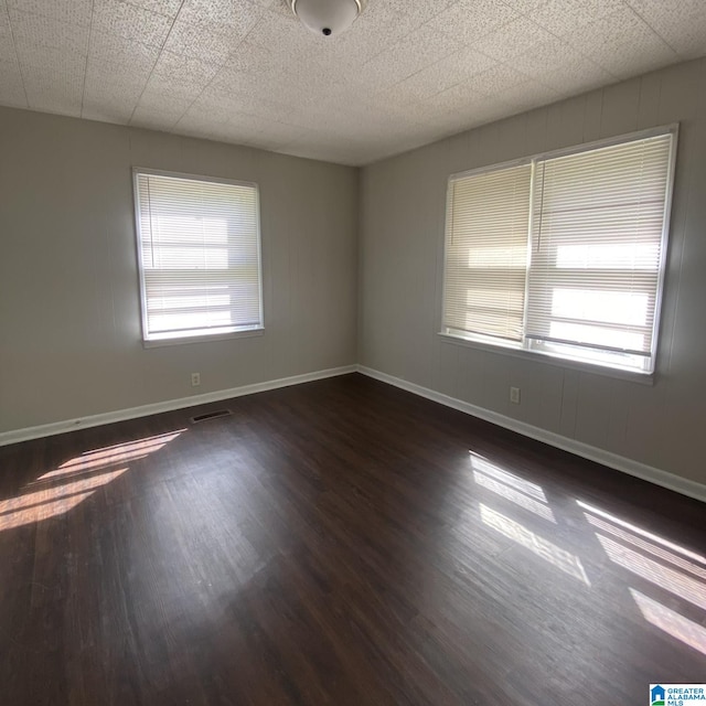 unfurnished room with a drop ceiling, plenty of natural light, and dark wood-type flooring