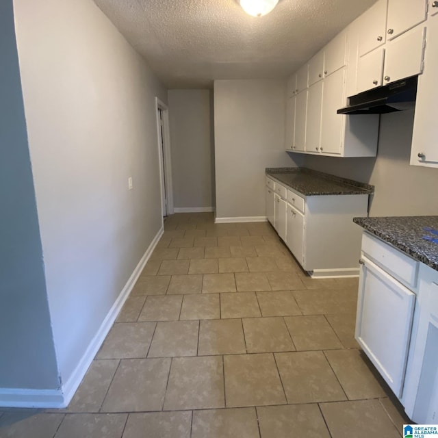 1121 Skyline Dr, Birmingham, AL 35214 - kitchen with dark stone counters, a textured ceiling, white cabinetry, under cabinet range hood, and baseboards