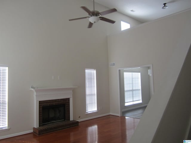 unfurnished living room with a fireplace, a towering ceiling, ceiling fan, and hardwood / wood-style flooring