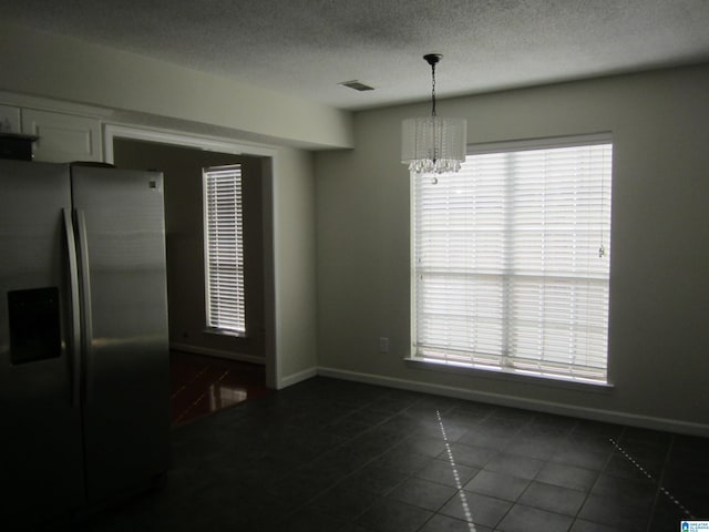 interior space with a textured ceiling, an inviting chandelier, dark tile patterned floors, and plenty of natural light