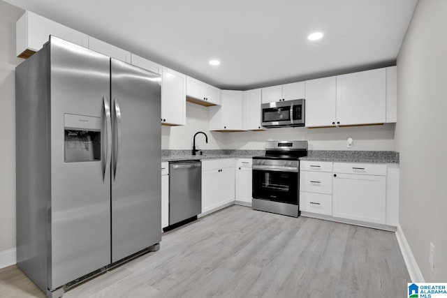 kitchen with light stone countertops, sink, light hardwood / wood-style floors, white cabinetry, and appliances with stainless steel finishes